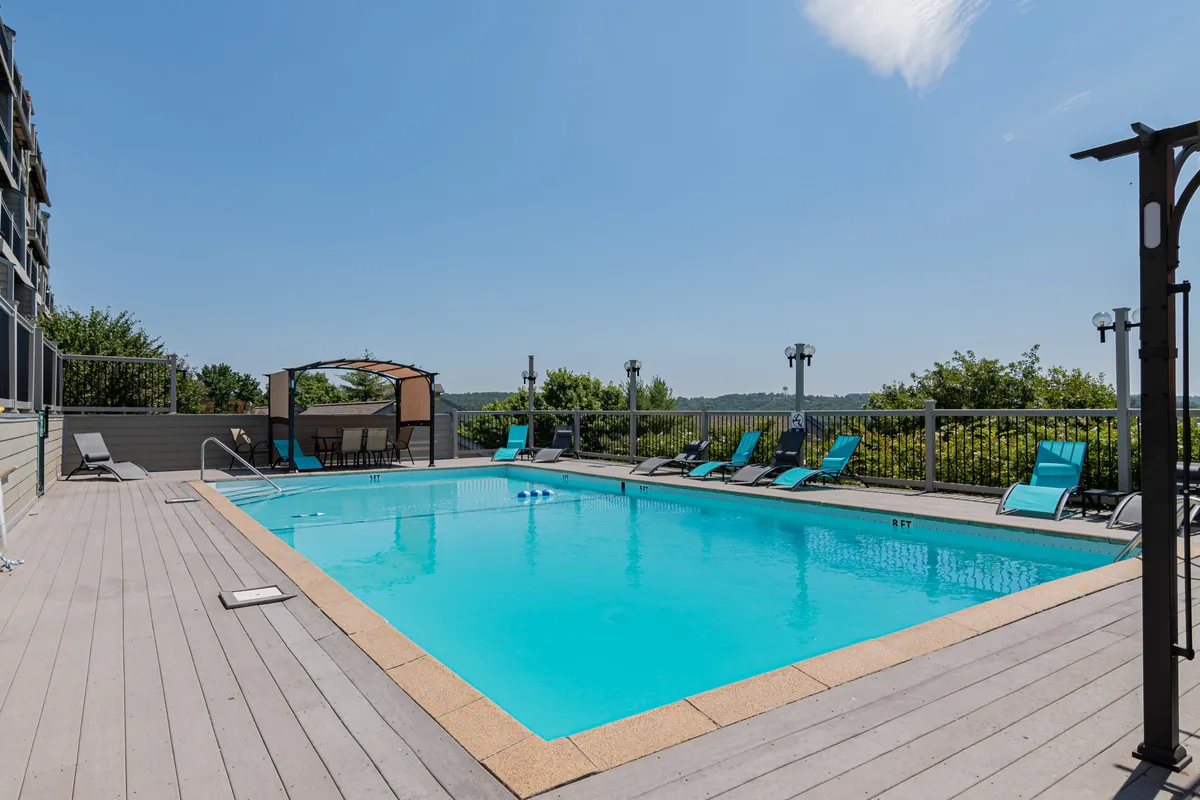 An outdoor swimming pool surrounded by lounge chairs and a canopy area, set against a scenic landscape. The pool is inviting and designed for leisurely swims, socializing, and relaxation. The area is perfect for both families and friends to gather and enjoy the summer sun.