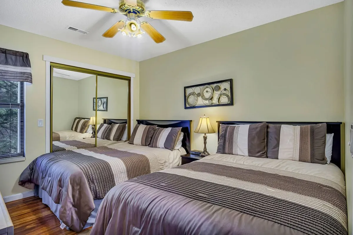 A welcoming second bedroom with two full-size beds, a central nightstand with a lamp, and a mirror on the wall. The arrangement is ideal for siblings, kids, or friends, offering both comfort and togetherness for a family retreat.