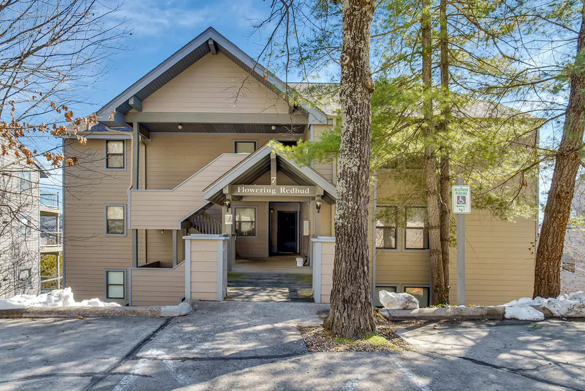The image highlights the entrance to the 'Flowering Redbud' building, framed by trees and architectural details. The peaceful surroundings and accessible entrance evoke a sense of welcome and retreat.