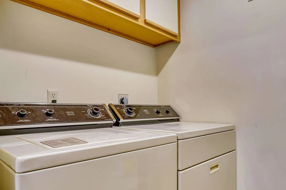 This image shows a dedicated laundry area with a full-size washing machine and dryer, along with a storage cabinet above. The space is neat and practical, suggesting convenience for guests who need to refresh towels and clothing during their stay.