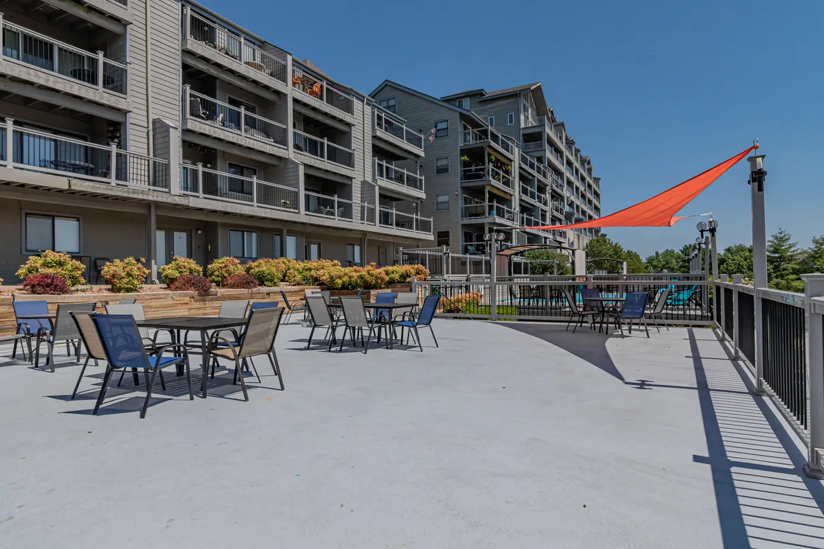 An inviting exterior space with a sunshade structure, colorful flowers, outdoor seating, and balconies overlooking the area. The setup encourages relaxation, socializing, and soaking in the outdoor ambiance.