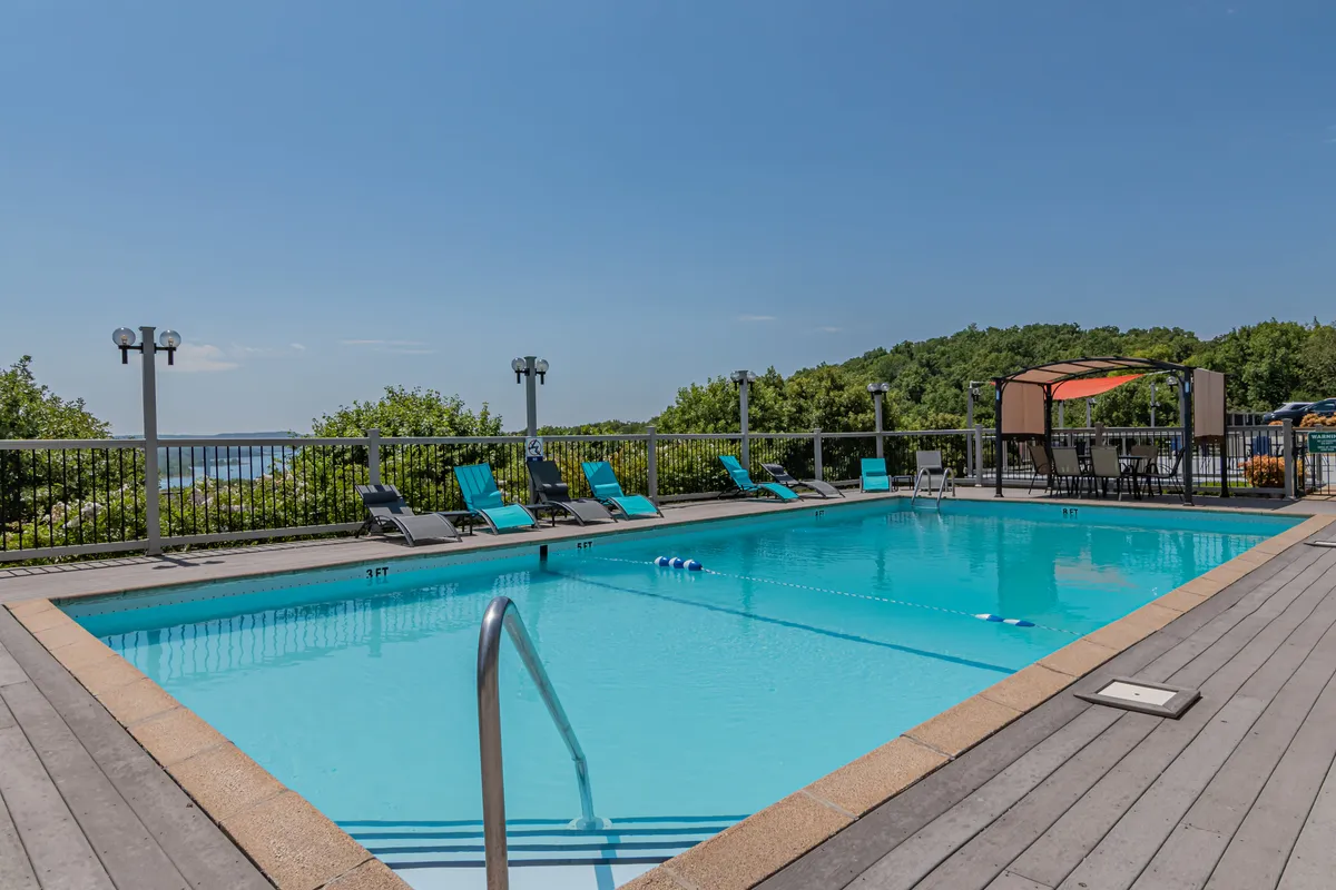 This image features a sparkling swimming pool surrounded by lounge chairs and canopy seating, set against a pleasant landscape backdrop. The pool area is inviting for guests to relax, sunbathe, socialize, or enjoy a refreshing swim on a warm day.