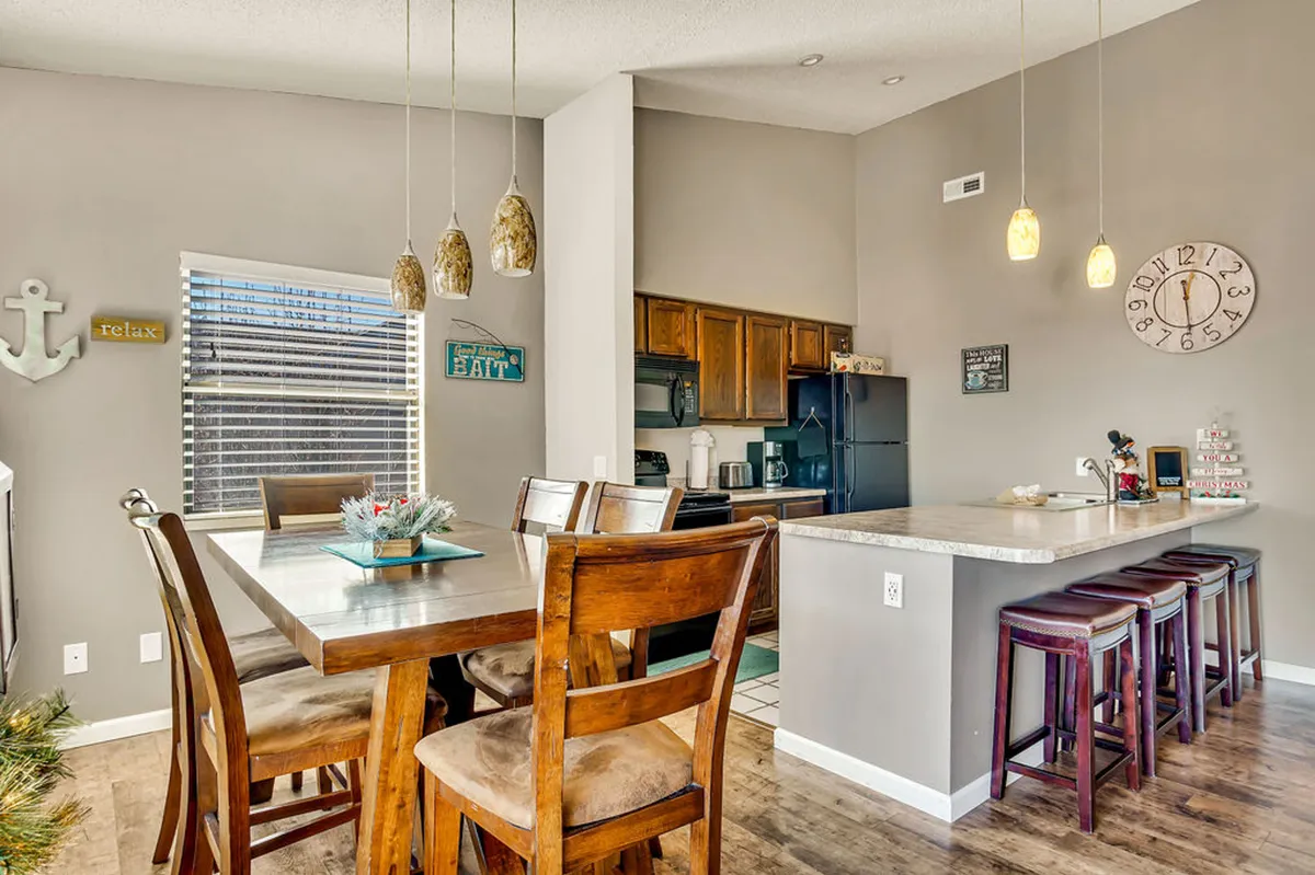 A spacious, cozy dining area with a large table under modern pendant lights and a nearby kitchen island, ideal for group meals, morning coffees, or entertaining friends after a day of exploring local attractions.